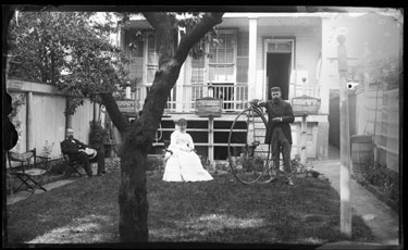 USA: View of back garden looking onto house and back porch with two men and a woman