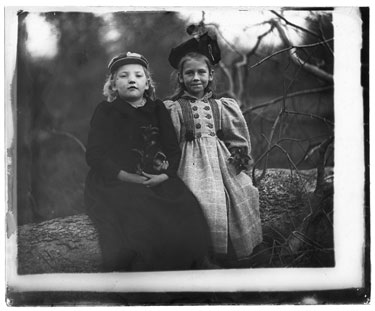 Unknown: Two girls sat on a fallen tree in long Winter coats and hats