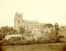 View: c09900 A view of Bunbury Church from the bottom of an incline, the church is silhouetted against the sky with several old buildings in front, including a thatched cottage 